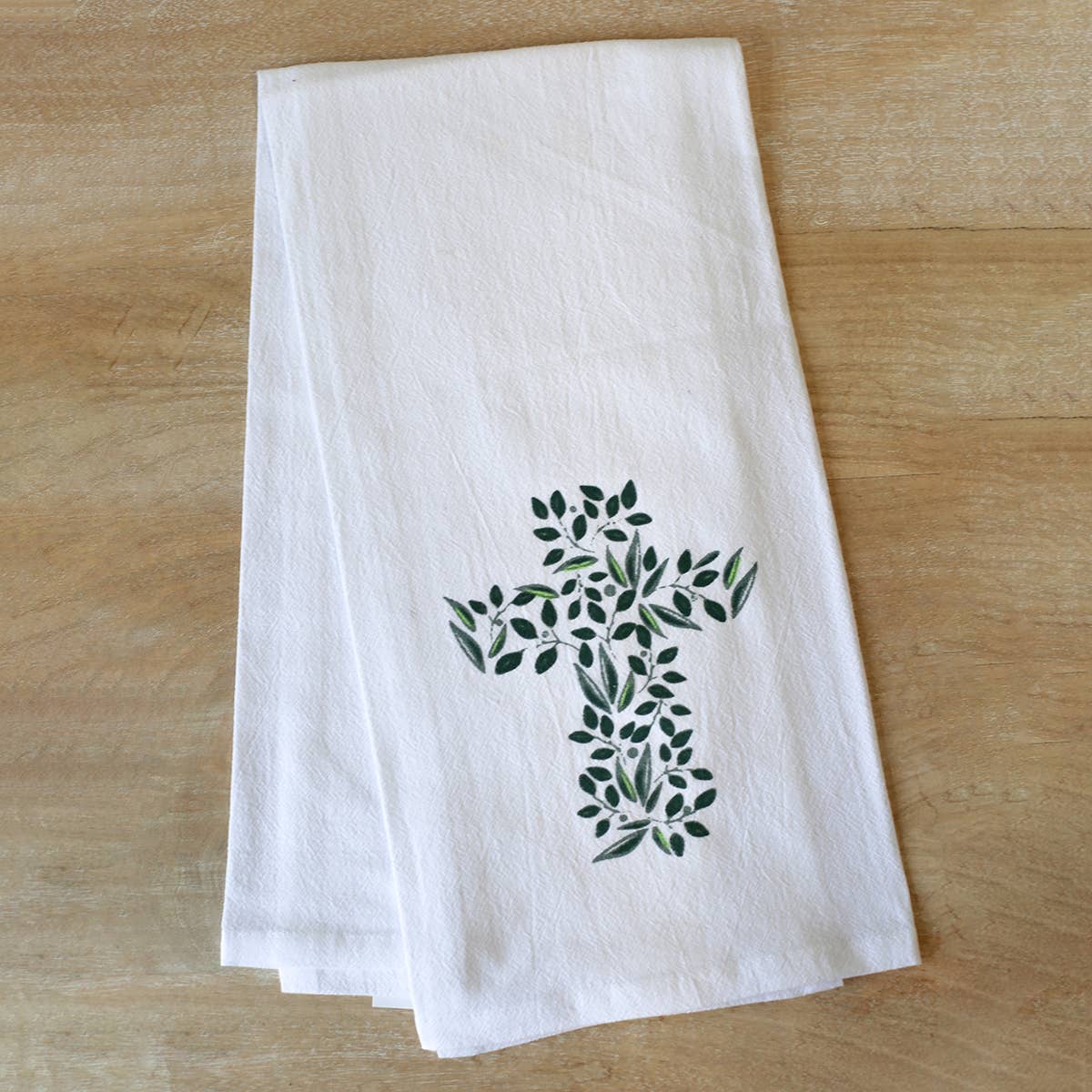 A hand towel featuring a cross out of greenery, folded in half, sitting on wood.