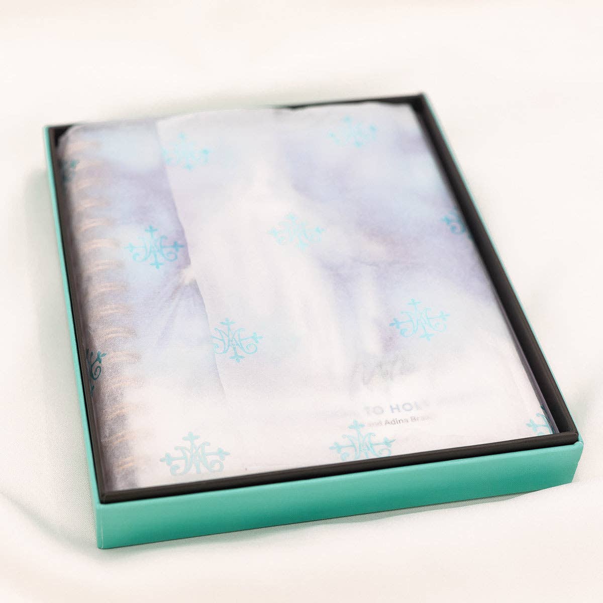 A turquoise box with a 40-Day Devotional to Holy Habits, "Mother Mary, Mother Me" compiled by Amy D'Ambra and Adina Braatz from My Saint My Hero that is wrapped in white folded tissue covering the book.