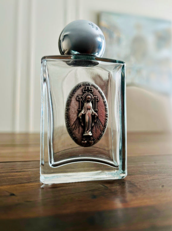 A glass holy water bottle featuring a silver Miraculous Medal.