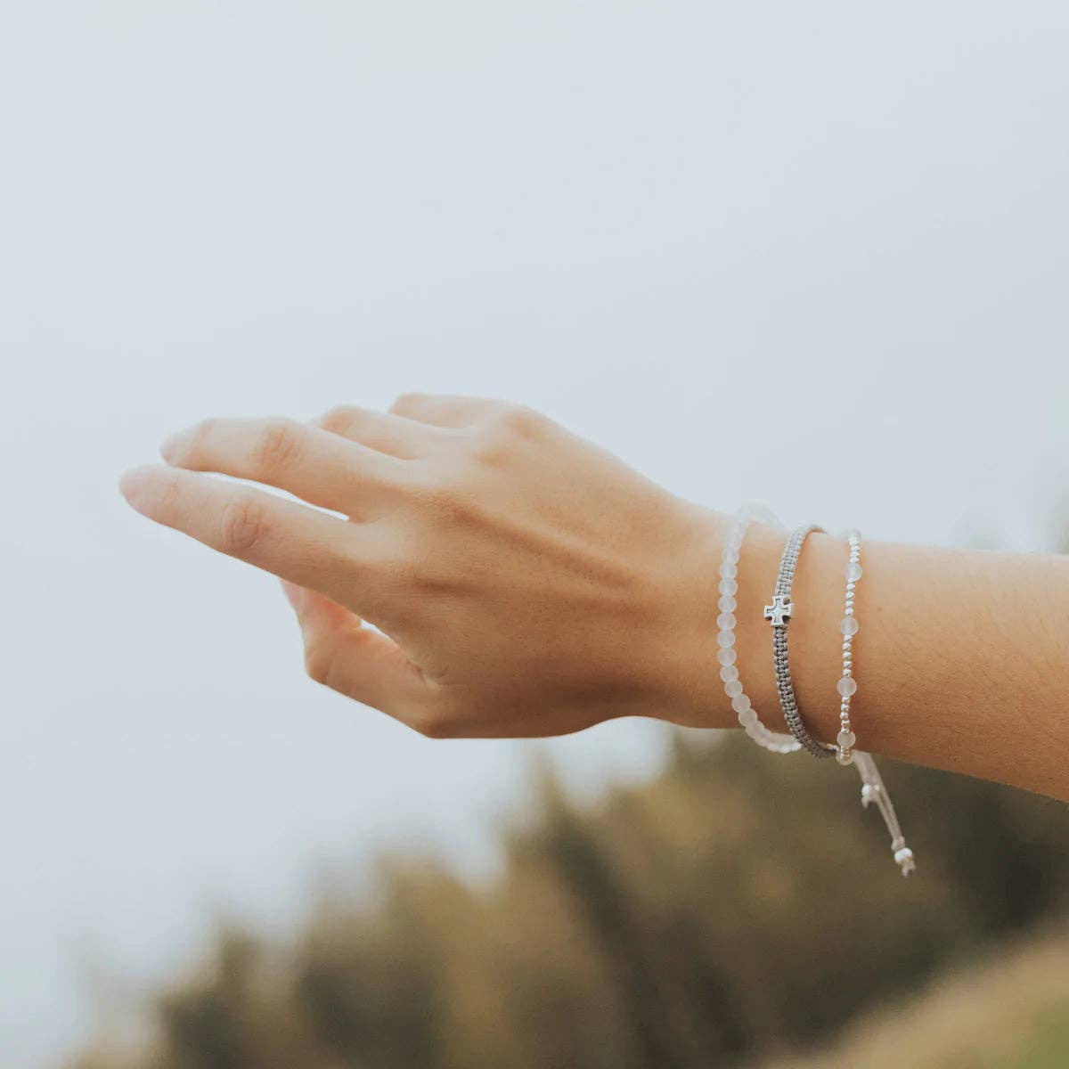 A women's hand and wrist, while she is wearing a Gray Frosted White, and silver triple pull bracelet featuring a silver cross.