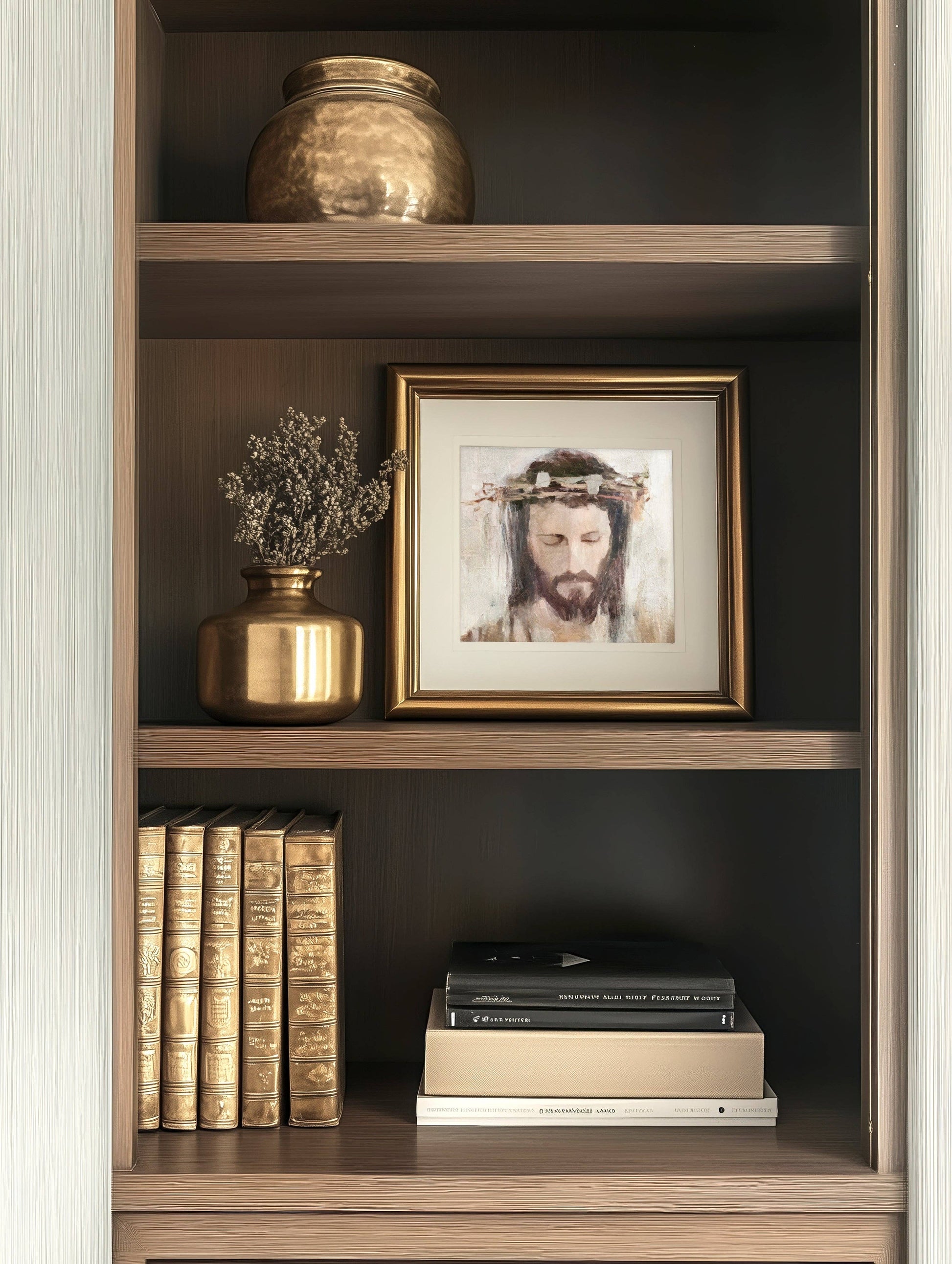 A bookshelf filled with books, two vases which include one filled with flowers, and a framed artwork featuring a Crowned Jesus in a gold frame.
