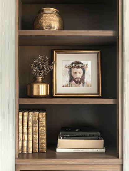 A bookshelf filled with books, two vases which include one filled with flowers, and a framed artwork featuring a Crowned Jesus in a gold frame.