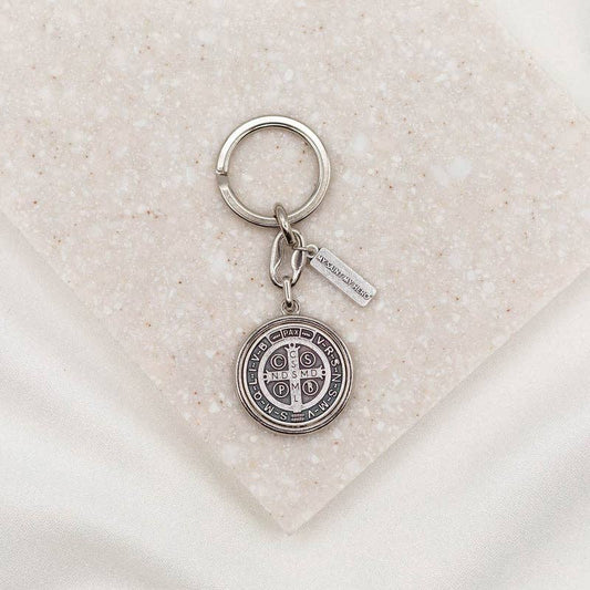 A silver Saint Benedict Keychain on a neutral stone backgound.