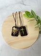 Brown Scapular featuring a green cross and brown heart with white flowers in the center and rays around the heart.
