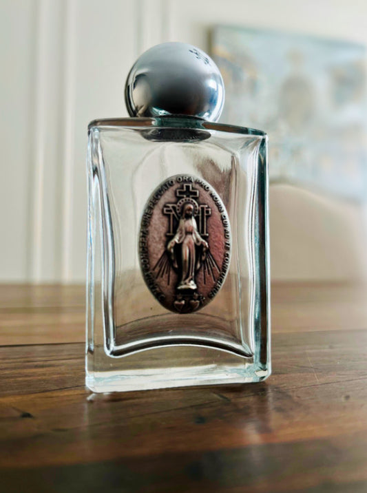 A glass holy water bottle featuring a silver Miraculous Medal.