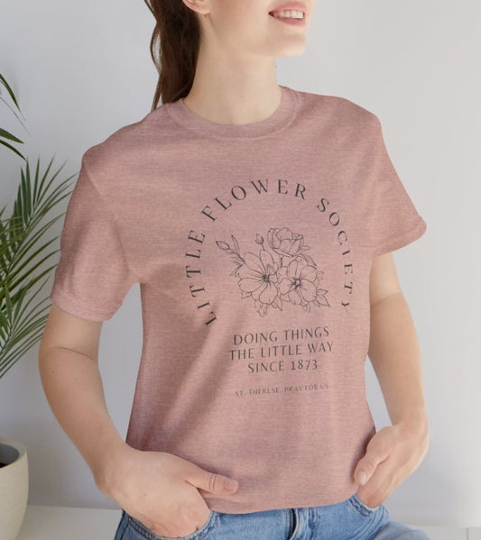 A heather pink shirt that reads "Little Flower Society" and "Doing things the Little Way since 1873" and "St. Therese of Lisieux, Pray for us." with a floral image in center.