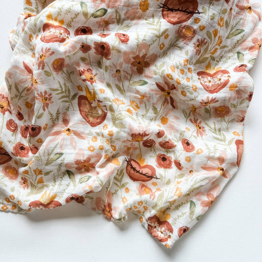 An open baby blanket with flowers and Sacred Heart whimsical designs.